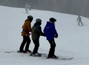 A skier learning how to slow down and stop with 2 ARISE & Ski training volunteers by their side.